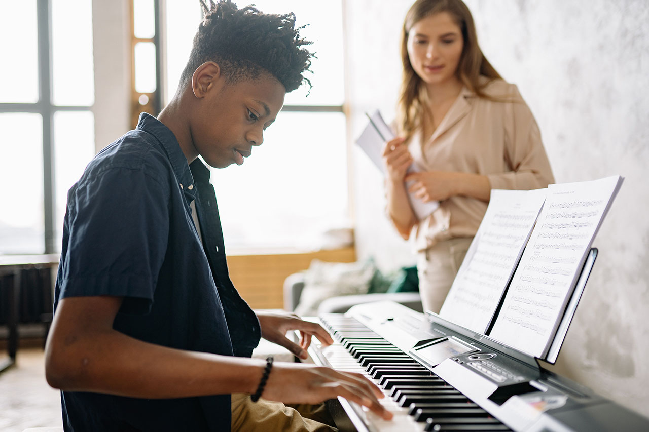 mentor watches while mentee practices playing piano