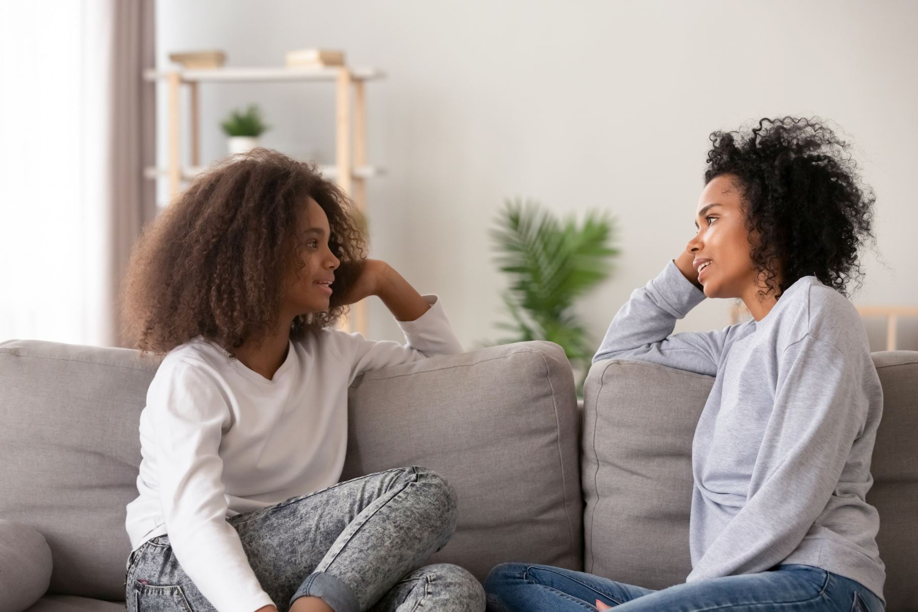 Black woman and teen girl sitting on the couch together in face to face conversation