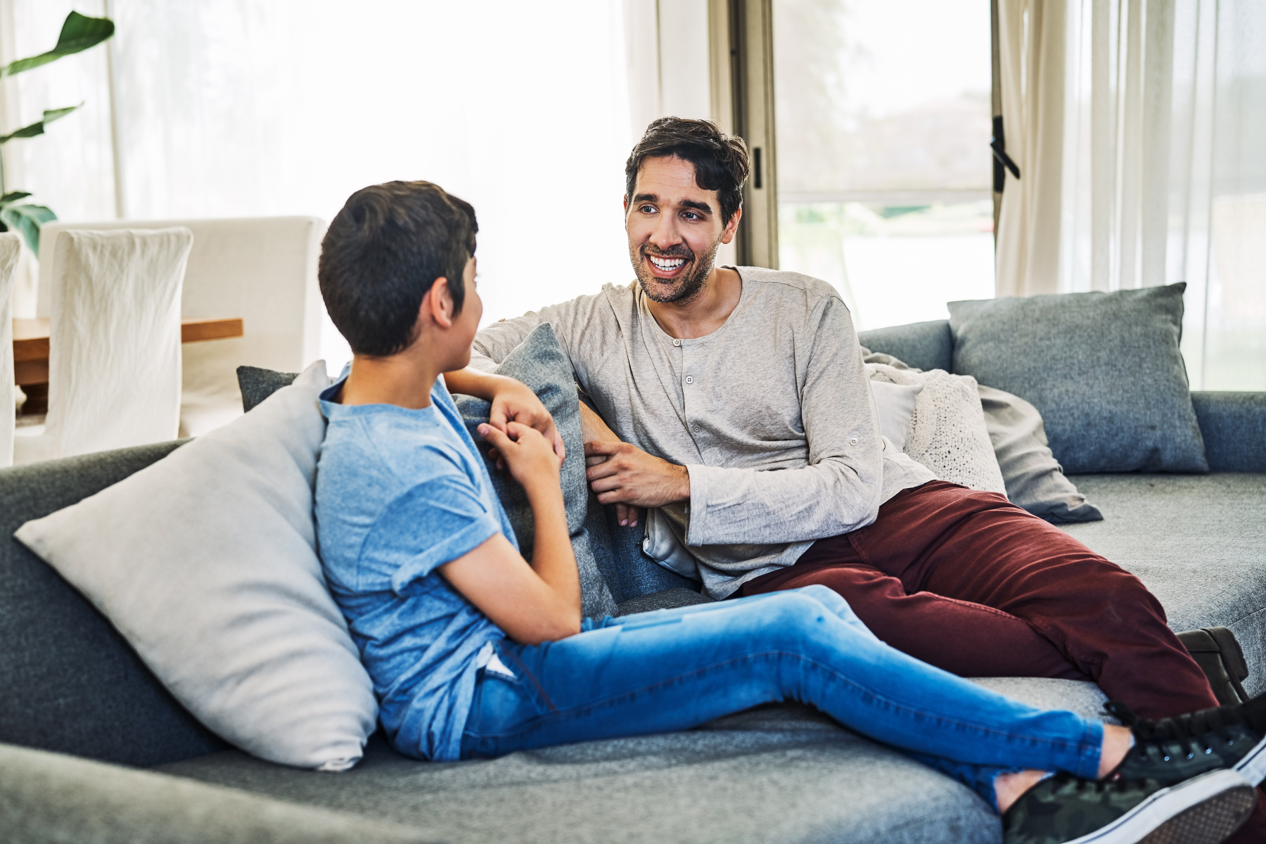 man and young teen sit together in conversation on a living room couch
