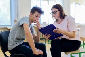 male teen talking to female adult in classroom looking at clipboard