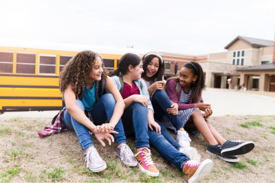 diverse small group of teen girls sitting on the ground and talking together in front of the schoolbus dropoff area