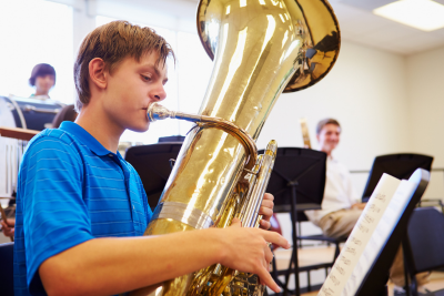 closeup of a white teen boy playing a tuba in band rehearsal