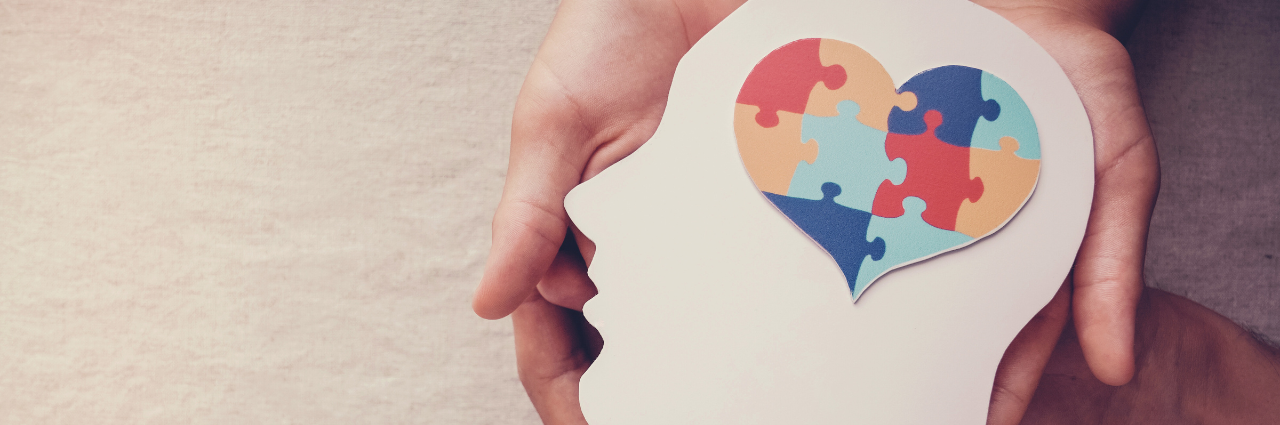 Hands holding paper cutout of head with a brain in the shape of a heart