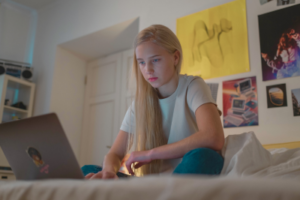 teen girl sitting on bed looking at laptop
