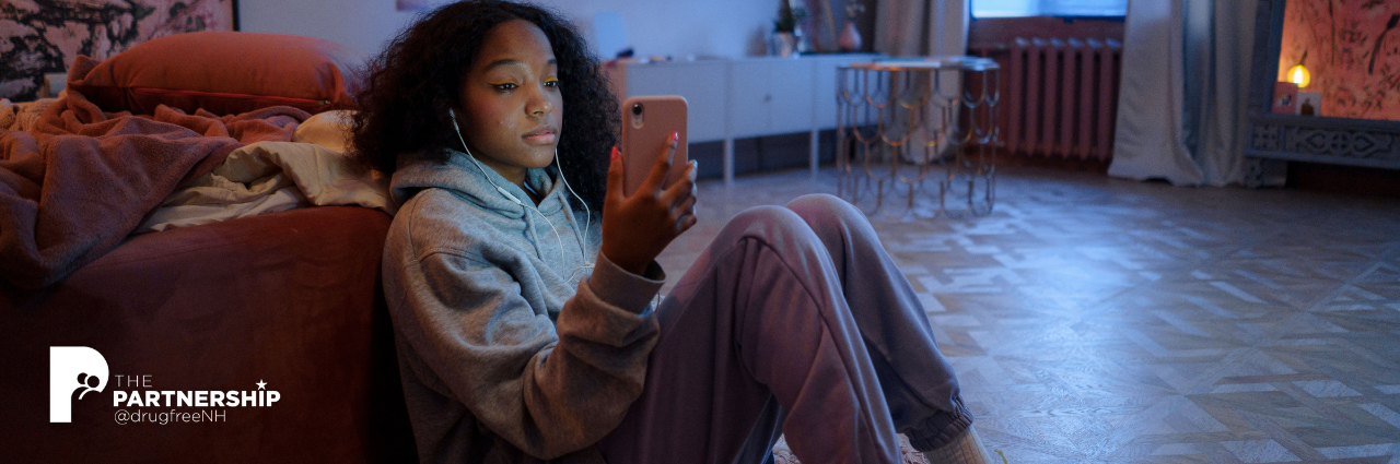 teen girl sitting on the floor while looking at a phone screen and wearing earbuds